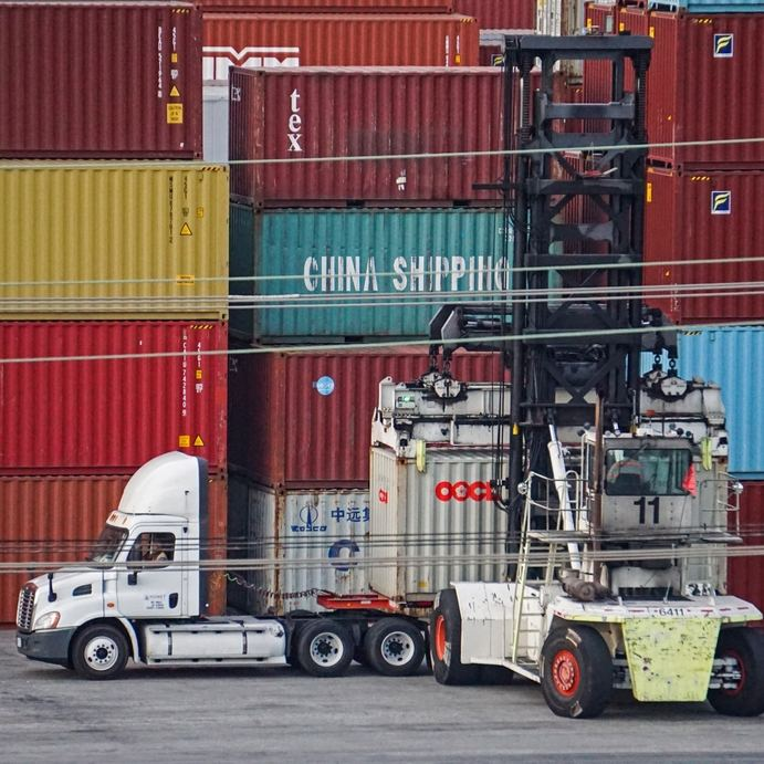 Container truck at port terminal with stacked shipping containers and crane